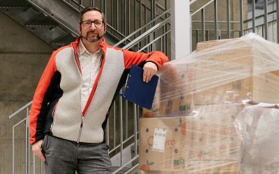 Mitarbeiter mit Brille und Klemmbrett neben verpackter Palette, Brillen ohne Grenzen Sponsoring