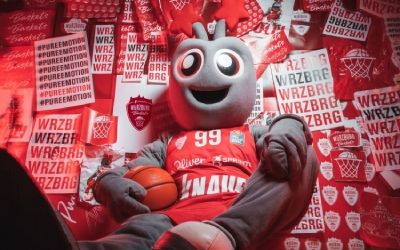 Basketball Maskottchen mit Ball vor rotem Hintergrund