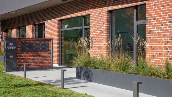 Firmeneingang von SPRINTIS mit Backsteinfassade, Glasfront, Briefkasten und bepflanztem Vorbereich